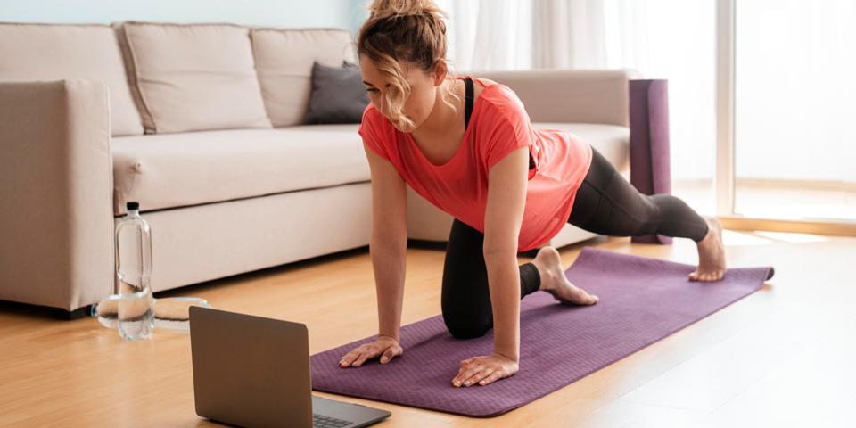 mulher realizando exercício físico em casa, olhando para um computador